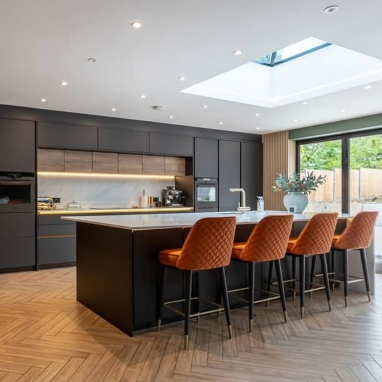 Contemporary kitchen with charcoal cabinets, a marble-top island, and rust orange bar stools under a skylight