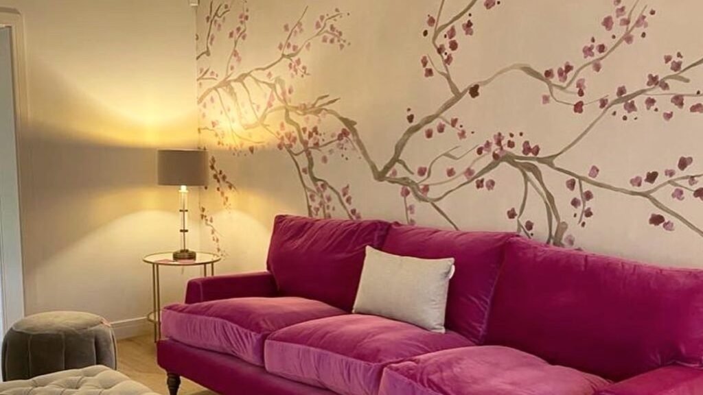Fuchsia velvet sofa against a hand-painted cherry blossom mural, an example of living room wall decor that skips framed art