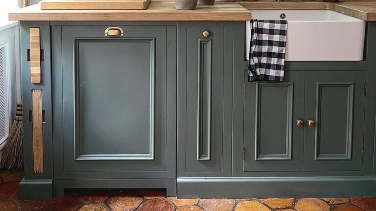 Country kitchen with deep green cabinets, terracotta hexagon tile floor, and open oak shelving holding stoneware pottery