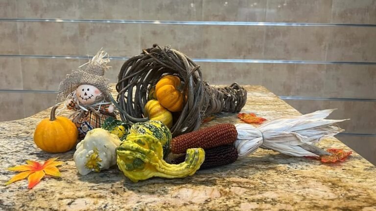 Thanksgiving cornucopia centerpiece with a burlap-hat scarecrow, mini pumpkins, ornamental gourds, and dried corn husks styled on a granite kitchen counter