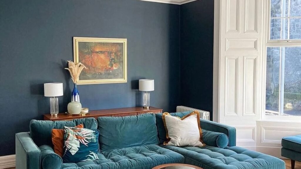 Living room with navy blue lower wall and white upper wall, teal velvet sectional sofa, gold chandelier, and dark hardwood floors