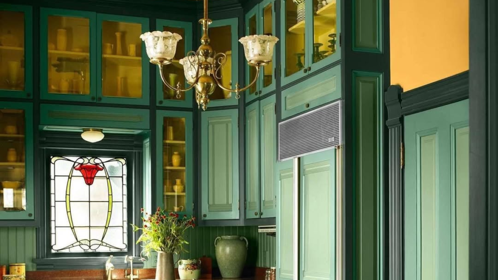 Dramatic Victorian kitchen with deep green paneled cabinetry, stained glass window, and antique carved dining chairs