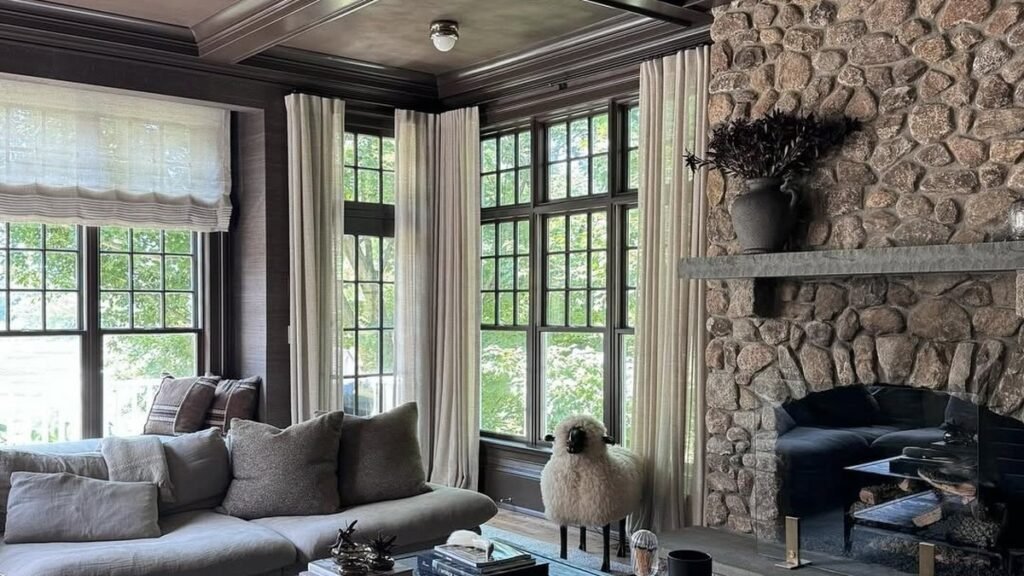 Sheer curtains layered over woven roman shades in a living room with a stone fireplace and dark coffered ceiling, part of 14 living room window treatment ideas