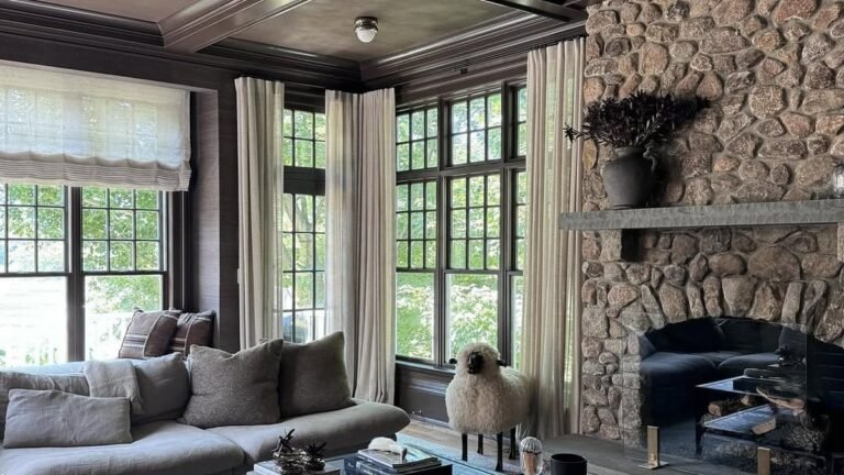 Sheer curtains layered over woven roman shades in a living room with a stone fireplace and dark coffered ceiling, part of 14 living room window treatment ideas