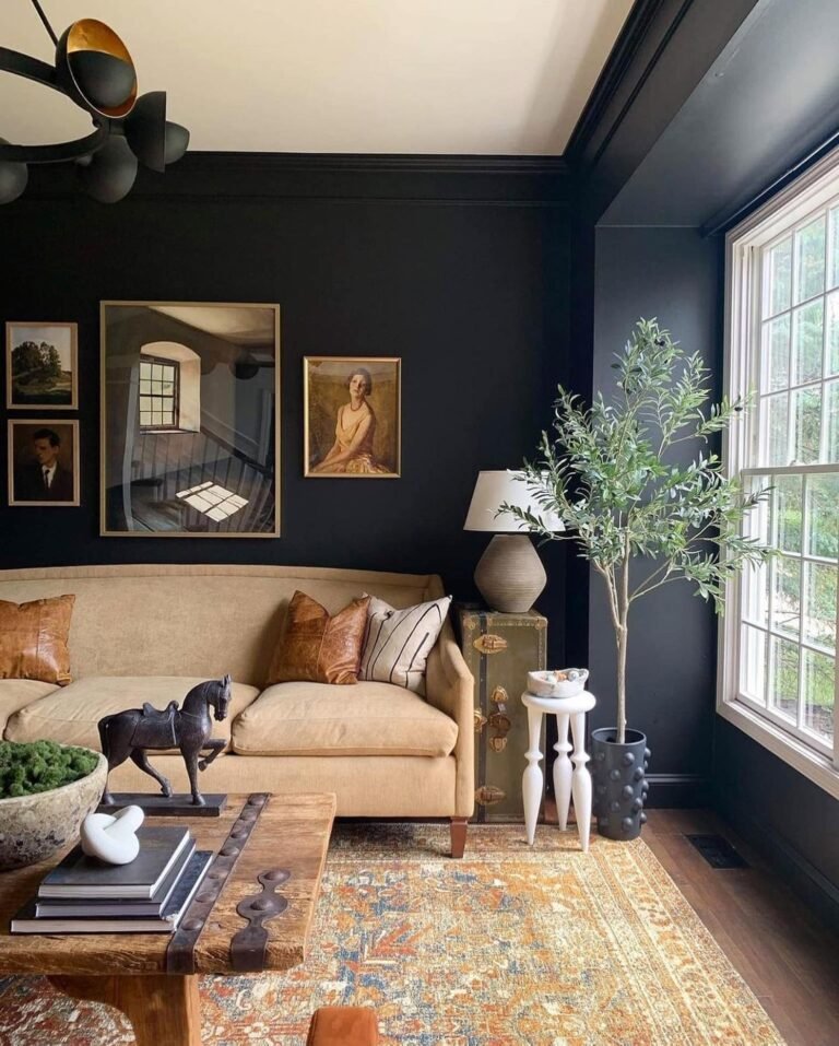 Living room with black-painted walls and trim, a tan sofa with leather cushions, a framed gallery wall, an olive tree by the window, and a warm patterned rug.