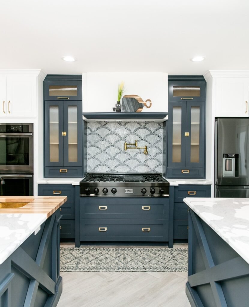 Navy blue kitchen cabinets with scalloped mosaic tile backsplash, gold pot filler, and white marble countertops