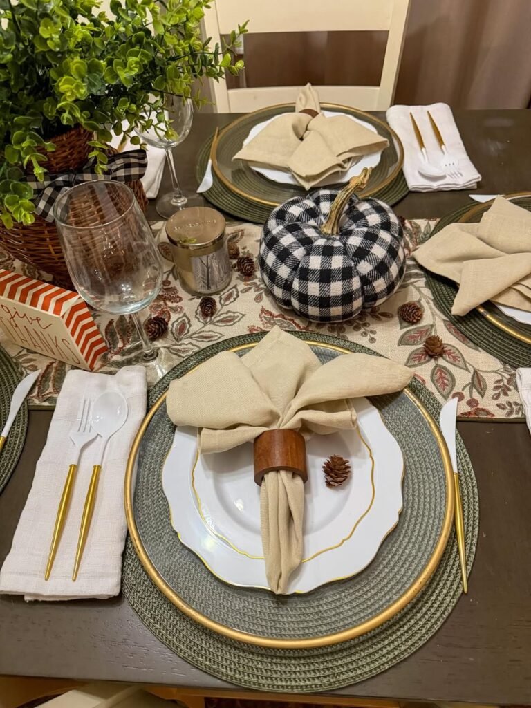 Black and white buffalo check pumpkin centerpiece on a Thanksgiving table with gold-rimmed plates and neutral linens