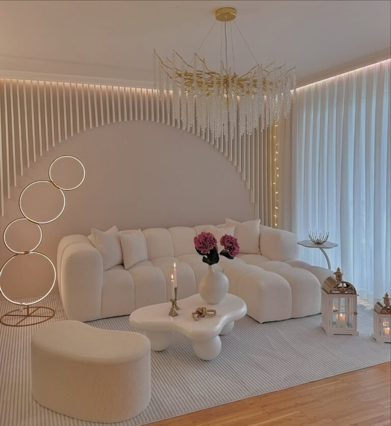 Living room lit by a cascading crystal branch chandelier, a glowing circular floor lamp, and a warm backlit curtain wall, with a white bouclé sofa and lanterns layering soft light at several heights instead of one overhead fixture.