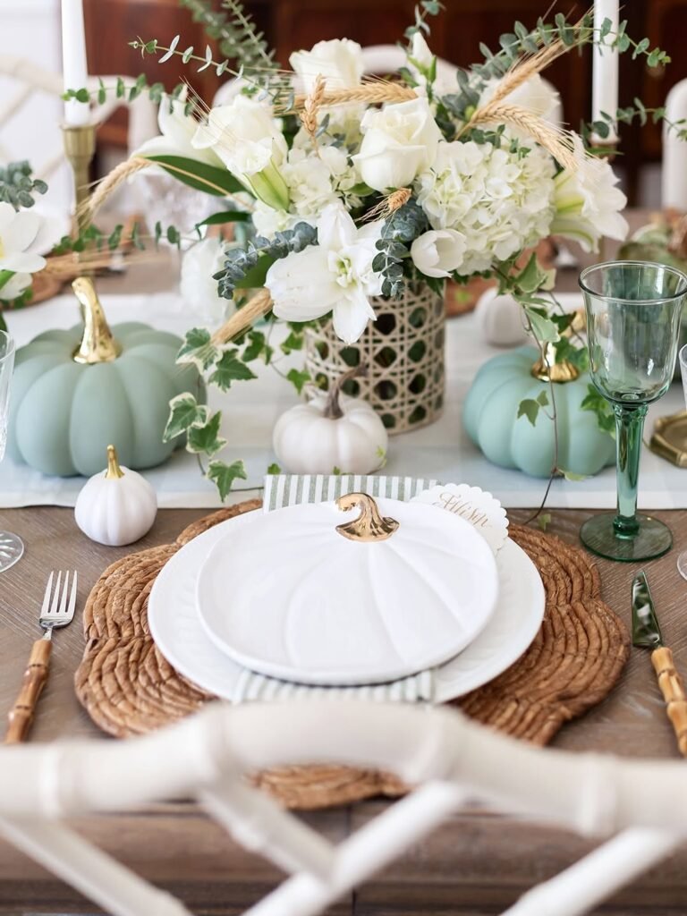 Thanksgiving table setting with a turkey-print plate, sage and white pumpkins, and a green glass goblet on a woven placemat