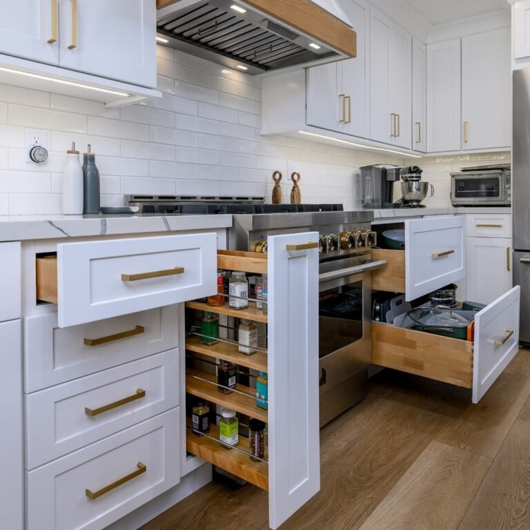 Built-in kitchen storage with three drawers open at once around a pro range, showing a vertical spice rack, deep pot drawer, and wide pan pull-out with white shaker fronts and gold pulls