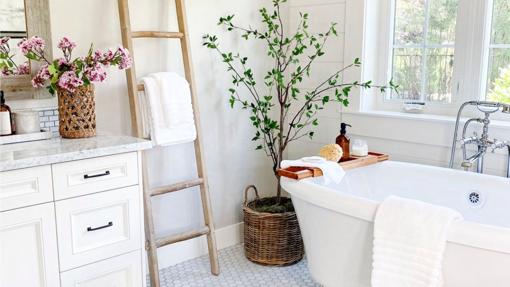 White farmhouse bathroom with a clawfoot soaking tub, wooden ladder towel rack, potted birch tree, and marble vanity