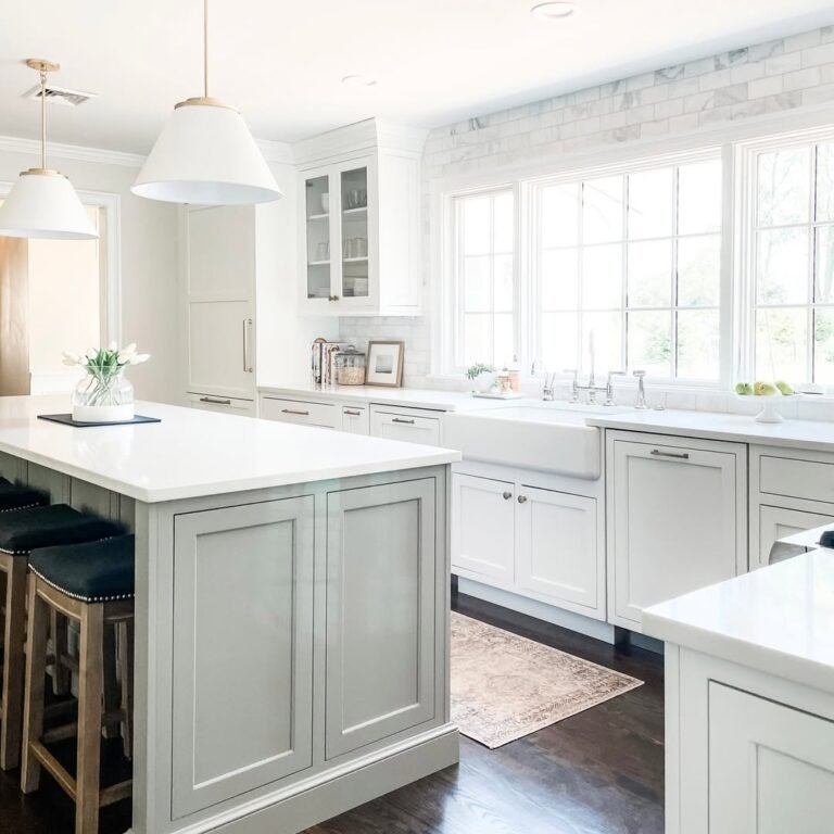 Bright white kitchen with sage green island and a full wall of large windows letting in natural daylight