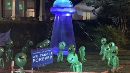 Green alien figures hauling a glowing blue UFO across a Halloween yard display at night