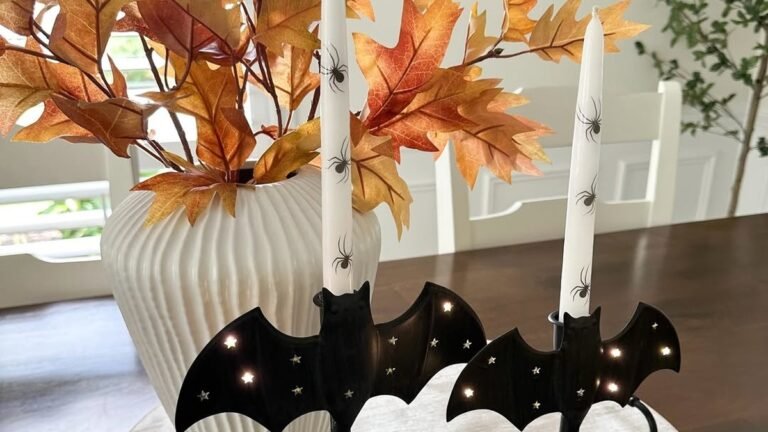 Two black bat-shaped candle holders with lit taper candles on a round whitewashed wood tray, styled with a white ribbed vase of autumn leaves for Halloween coffee table decor