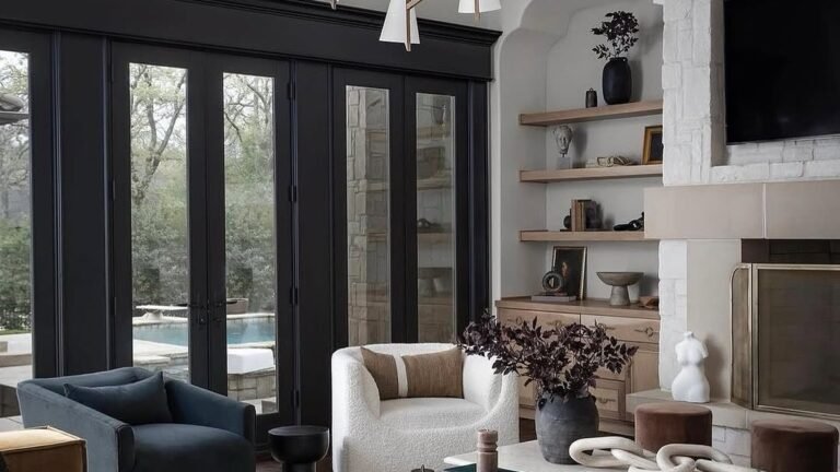 Modern living room with black steel-framed windows, a stone fireplace, mustard velvet sofa, and a navy swivel chair opening onto a pool view