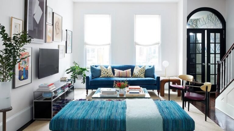 Narrow living room with a cobalt velvet sofa and matching striped ottoman, a low media console anchoring the long wall beneath a gallery of framed art