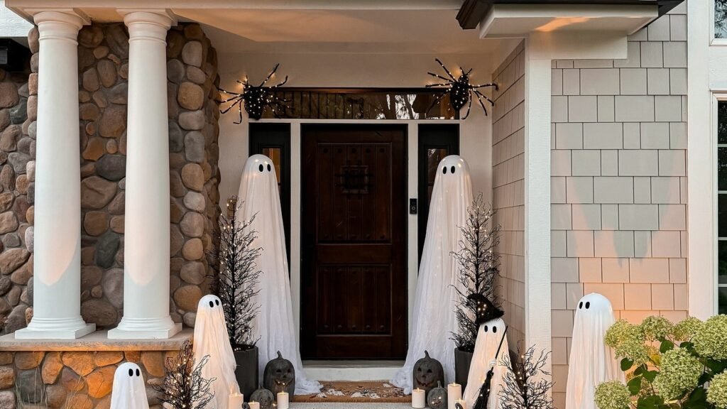 Ghost decorations and candles lining a stone porch staircase with spider silhouettes above the door