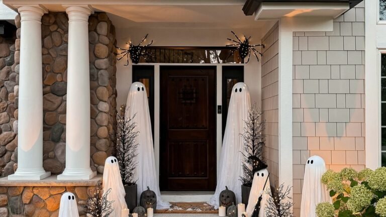 Ghost decorations and candles lining a stone porch staircase with spider silhouettes above the door