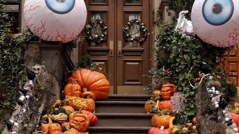 Two giant inflatable eyeball decorations hanging above a brownstone stoop staircase completely covered in orange, green, and white pumpkins and gourds for Halloween