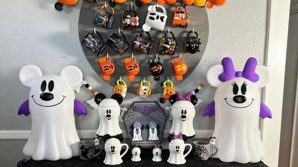 Ghost-shaped Mickey and Minnie Mouse figures in front of a Mickey Mouse silhouette wall covered in orange, black, and white Halloween coffee mugs