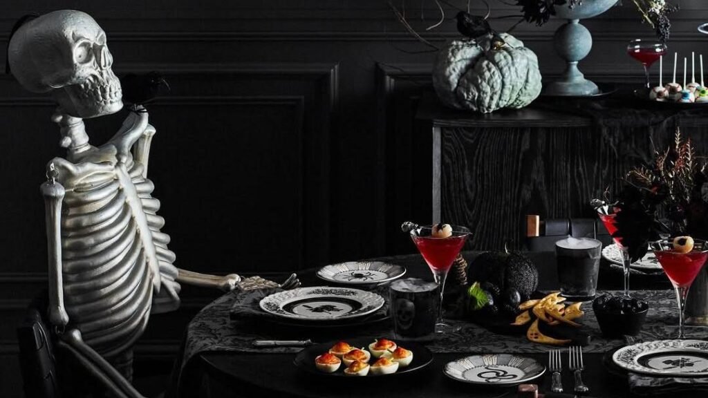 All-black Halloween dining room with a seated skeleton at the table, dark floral centerpiece, black and white spider plates, and red cocktail glasses