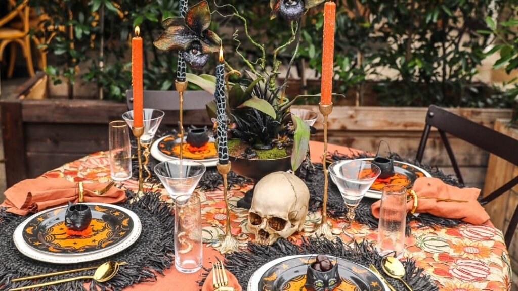 Halloween tablescape with orange linen, gold candlesticks, black and orange plates, and a skull centerpiece on an outdoor table