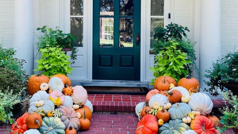 Two overflowing piles of orange, white, and blue-green pumpkins and gourds stacked on red brick steps leading to a teal front door, October home decor ideas