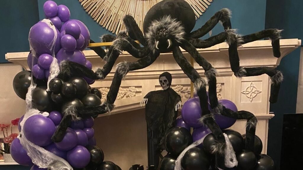 Purple, black, and orange balloon arch with a giant faux spider draped over a mantel for Halloween party decor