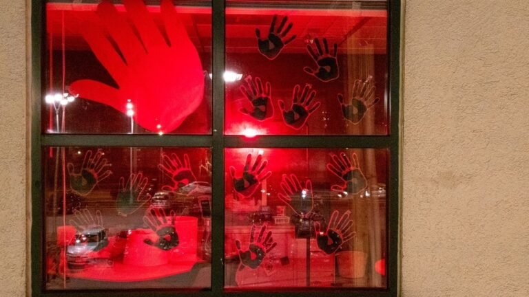 Halloween window covered in black handprint decals lit by red light from inside, with one oversized handprint on the corner pane