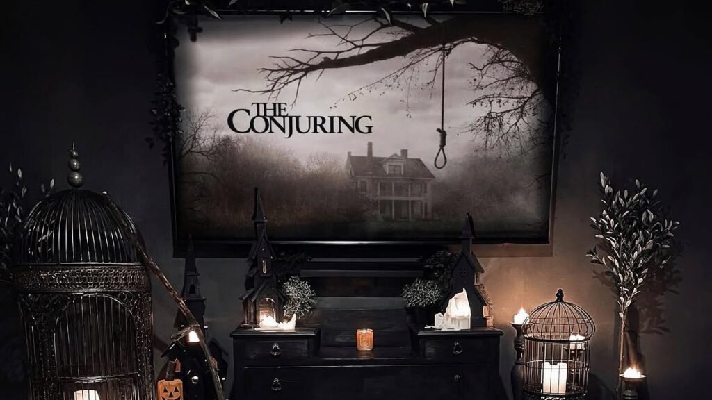 Dark gothic living room with The Conjuring movie poster above a black dresser, flanked by candlelit birdcages, styled as Halloween decor