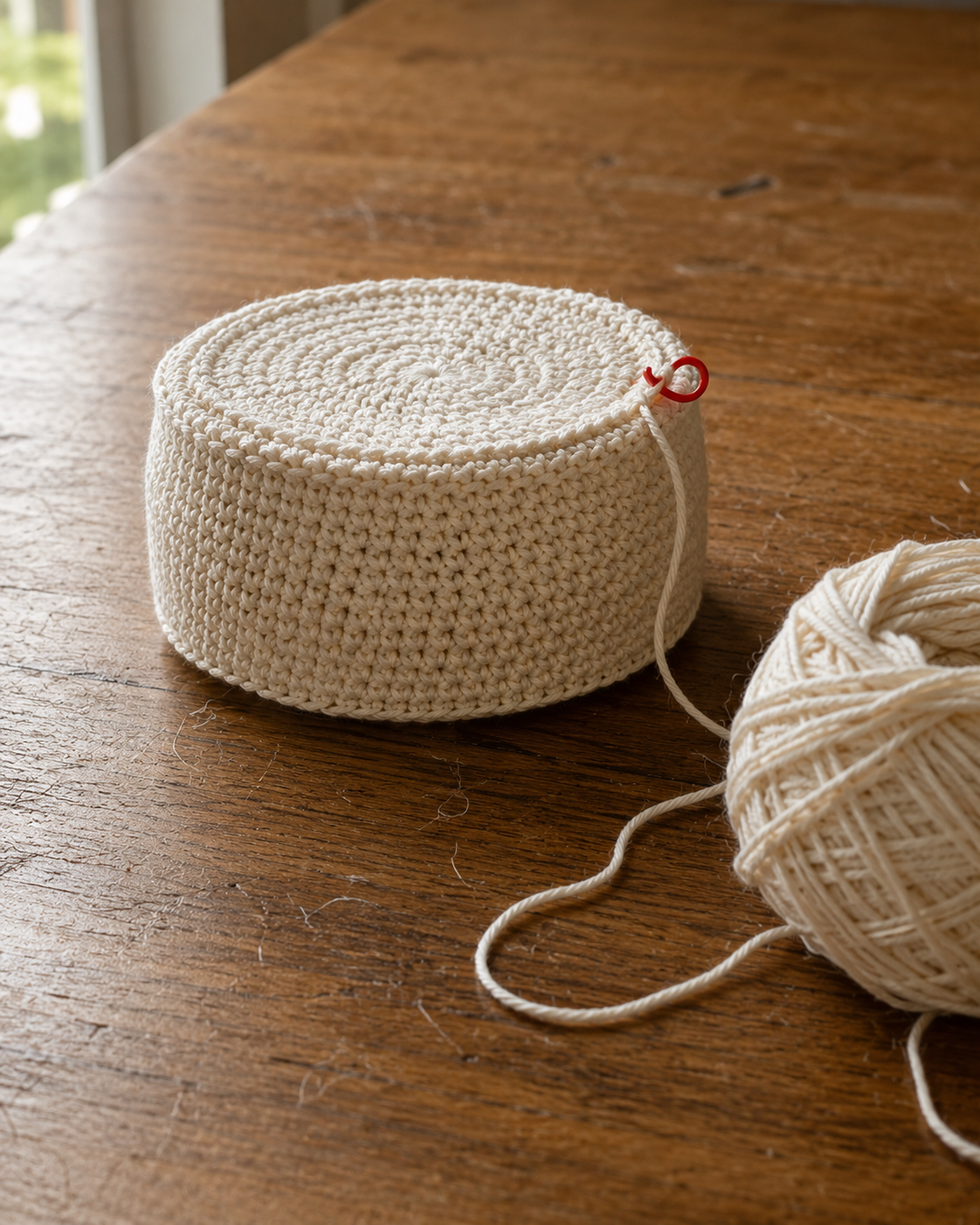 Crochet pumpkin body in progress with straight sides, red stitch marker and cream cotton yarn ball