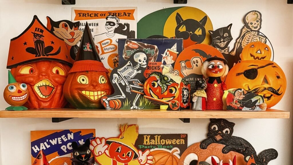 Vintage Halloween decor shelf with orange blow mold jack-o-lanterns, a tin litho skeleton, and a witch figure grouped together