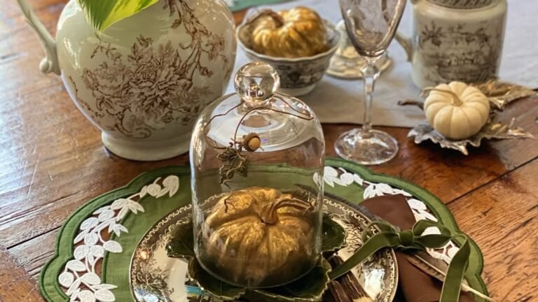 Gold pumpkin under a glass cloche on an elegant Thanksgiving table with a toile pitcher and white pumpkin