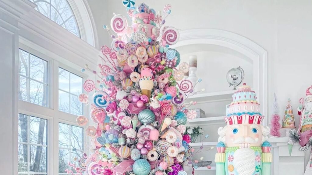 Pastel Christmas tree covered in pink, blue and mint lollipops, donuts and other candy ornaments beside a tall mint and pink nutcracker with a cake-shaped hat in a bright white room with arched windows.