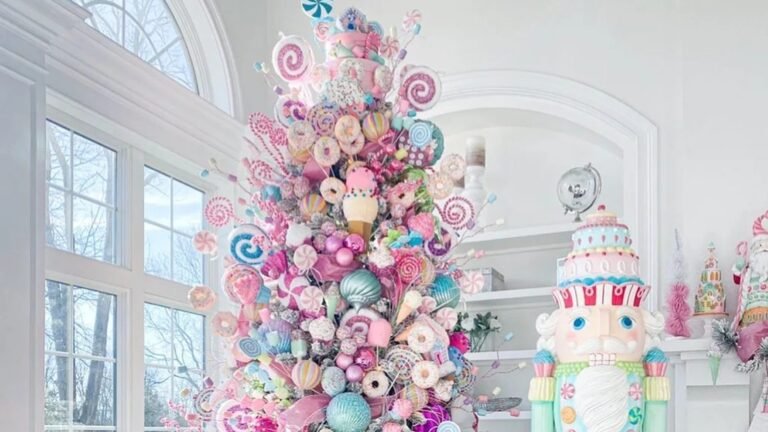 Pastel Christmas tree covered in pink, blue and mint lollipops, donuts and other candy ornaments beside a tall mint and pink nutcracker with a cake-shaped hat in a bright white room with arched windows.