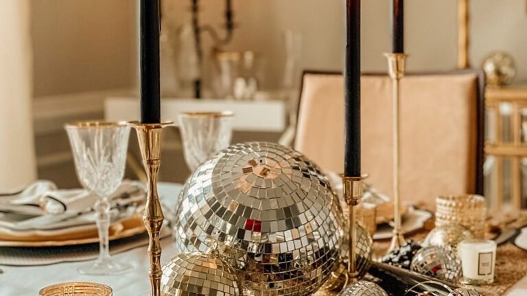 New Year’s Eve dining table centerpiece with large mirrored disco balls, tall black taper candles in brass candlesticks, crystal wine glasses, and a gold glitter runner.