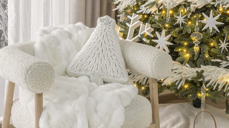 Textured cream armchair with a fluffy white faux fur throw and a tree-shaped pillow, set beside a Christmas tree with frosted white branches, snowflake ornaments, and warm string lights.