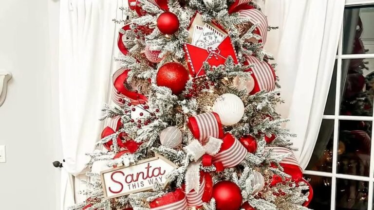 Flocked Christmas tree decorated with red and white striped ribbon, red and white ornaments, a red Letters to Santa envelope, and a wooden Santa This Way sign, in front of white curtains.