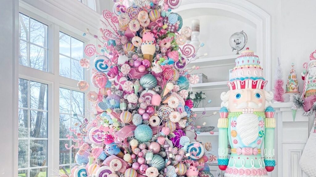 Tall flocked Christmas tree covered in pastel pink, blue, and mint lollipops, donuts, ice cream cones, and candy ornaments, standing beside a giant pastel nutcracker with a cake-shaped hat in a bright white room with tall windows.