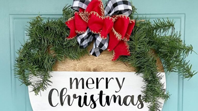 Round wood Christmas door sign with a white band reading merry Christmas, topped with a red and black-and-white buffalo check bow and green pine branches, hanging on a light aqua front door.
