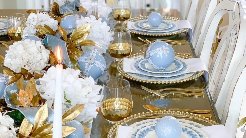 Christmas dining table decor with a light blue ornament set on each blue and white plate over gold beaded chargers, gold flatware, and a lit white taper candle beside white hydrangeas and gold leaves. I chose #24 (thespilledsugar) because three plates in a row each hold one ornament, which matches the title exactly. The pale blue and gold also stands out in a feed full of red and green.