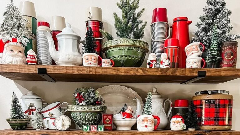 Two rustic wood open shelves filled with vintage Santa face mugs, red plaid thermoses and cooler, green ceramic bowls, a white teapot, and small flocked and bottle brush Christmas trees.
